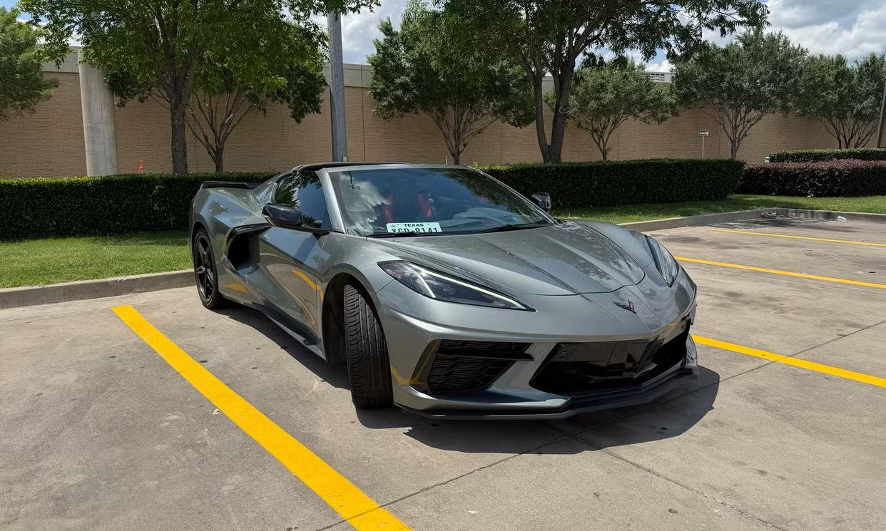 2023 Corvette Stingray profile view showing the open driver's door and mid-engine silhouette in a parking lot setting